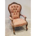 A late Victorian carved walnut button back salon chair, the waisted button back with a foliate