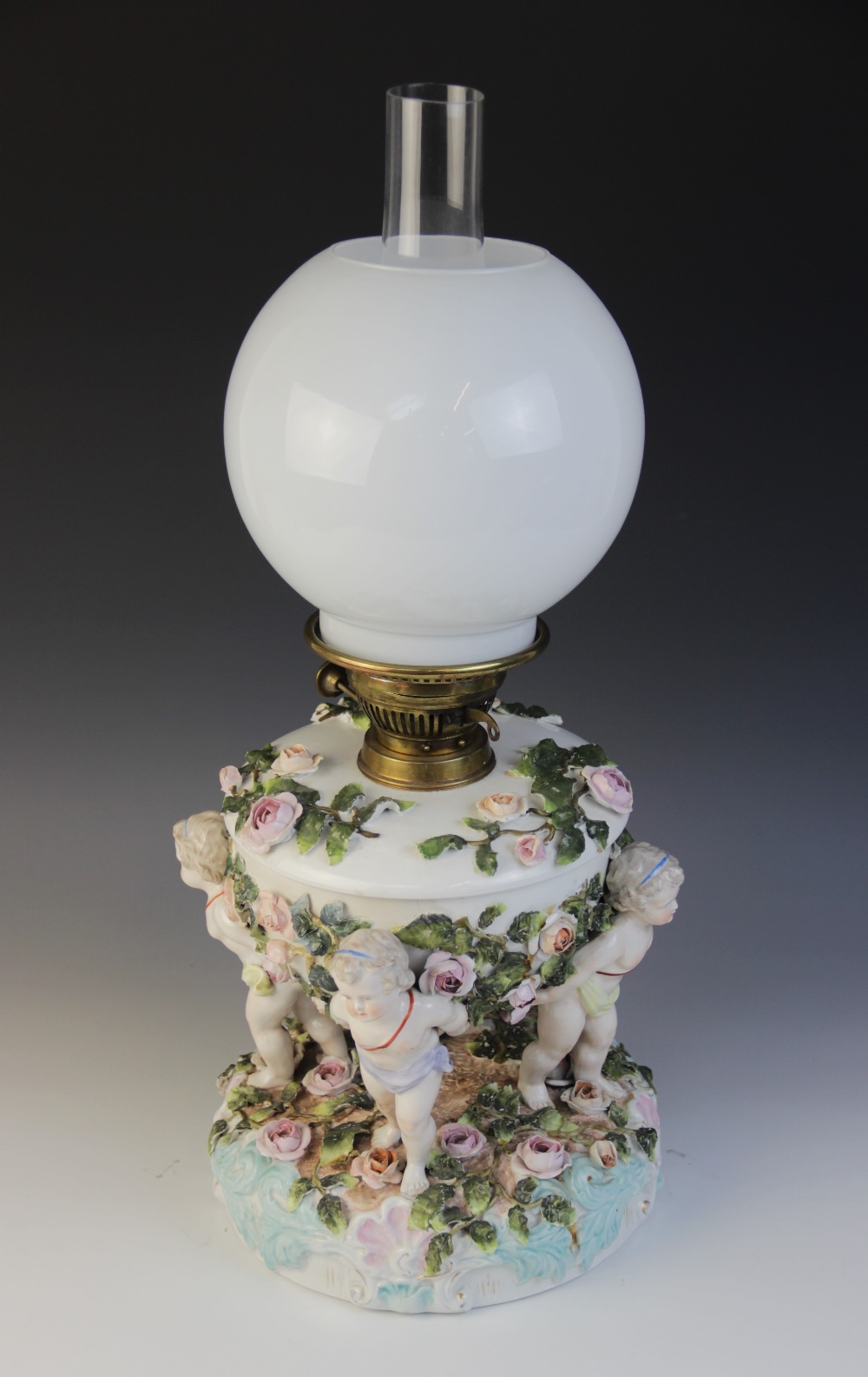 An German florally encrusted porcelain oil lamp, 19th century, modelled with four putti supporting