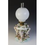 An German florally encrusted porcelain oil lamp, 19th century, modelled with four putti supporting