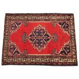 A hand woven wool carpet, with a central blue medallion against a vivid red ground, surrounded by