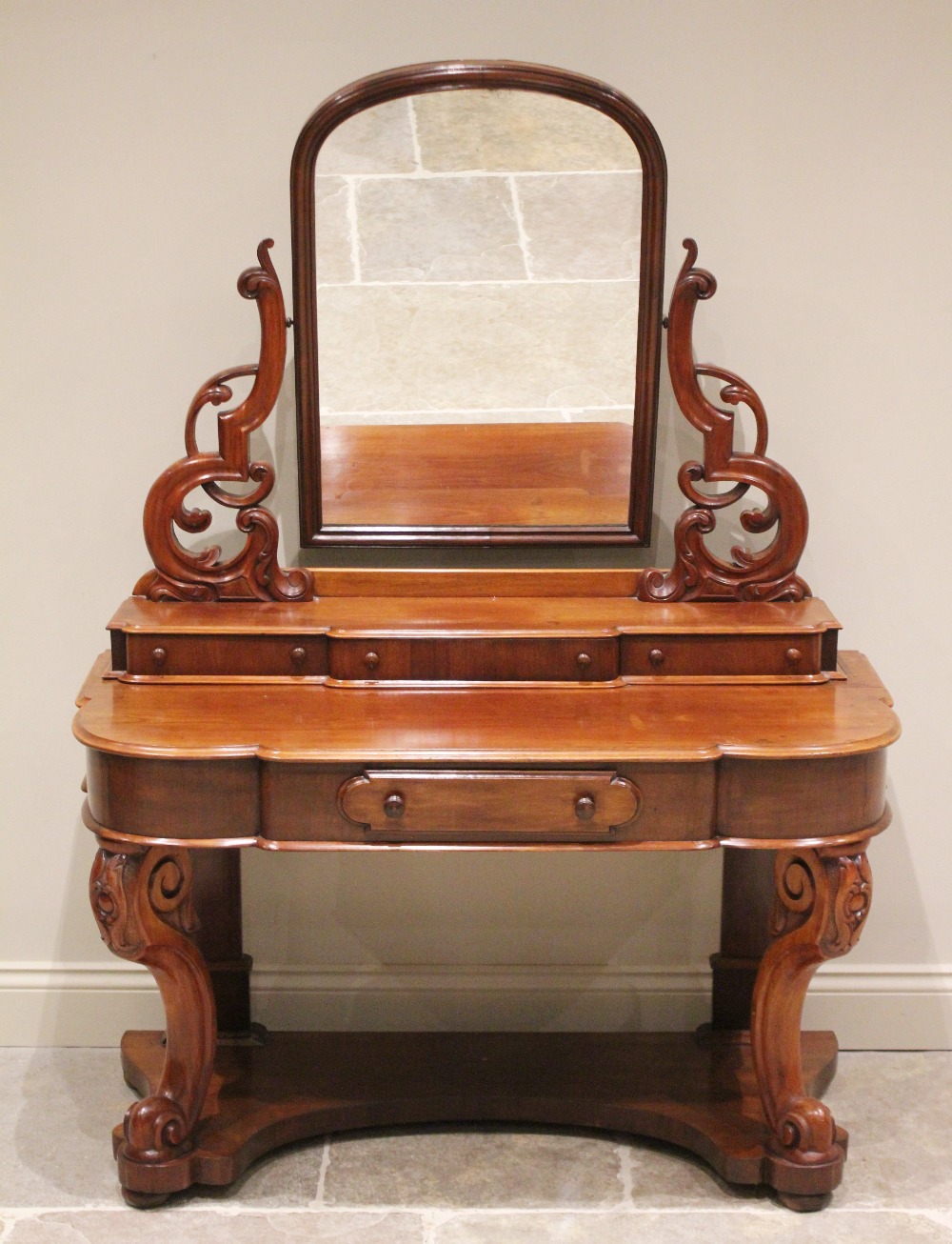 A Victorian mahogany Duchess dressing table, the arched swivel mirror raised upon scrolling open