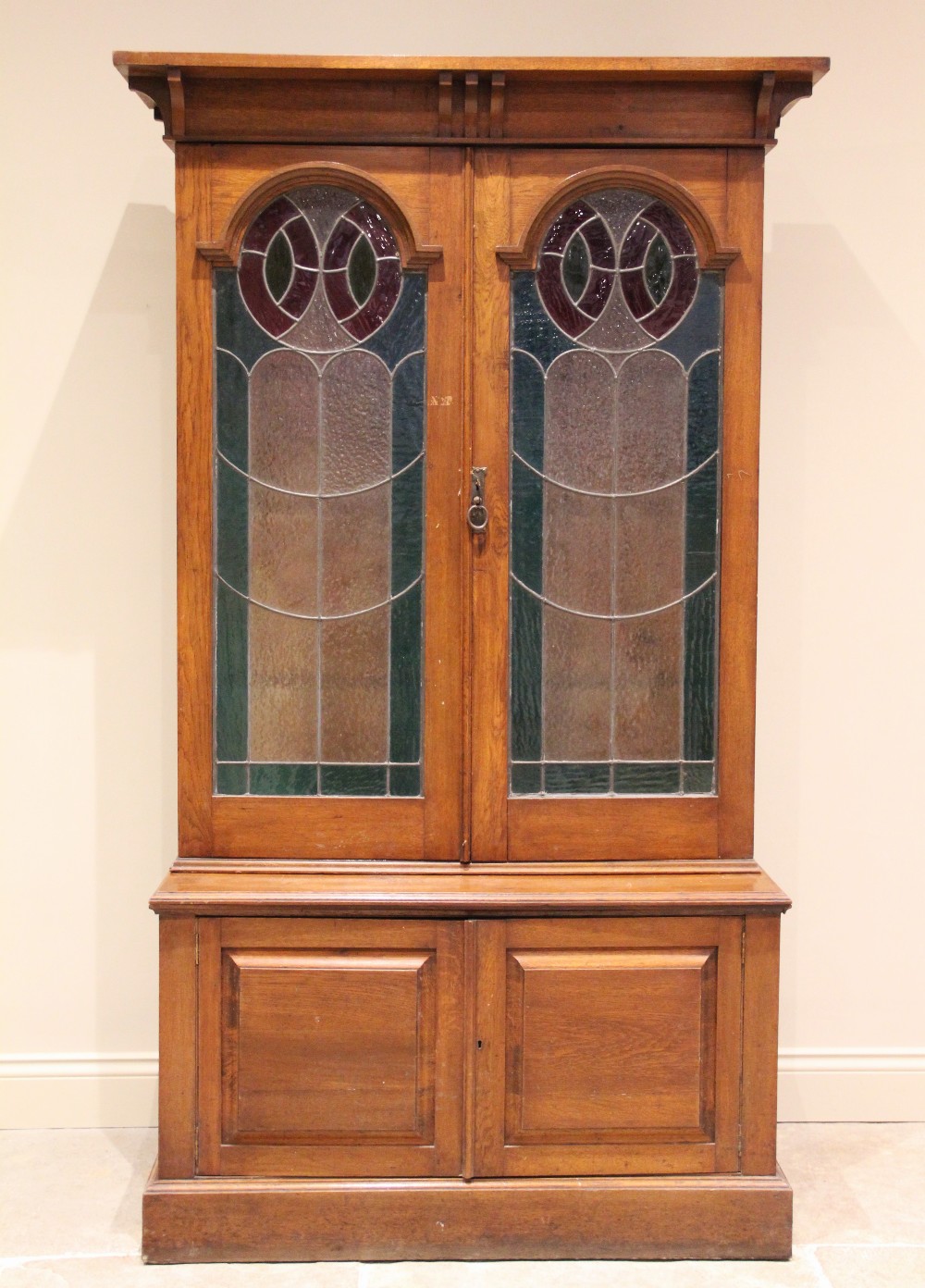 An early 20th century oak Arts and Crafts glazed bookcase, with an overhanging cornice above a
