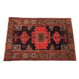 A hand woven wool carpet, with three geometric red panels against a dark ground, within a grey and