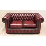 An oxblood red leather Chesterfield settee, late 20th/early 21st century, of typical deep set button