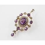 An Edwardian amethyst and seed pearl set pendant/brooch, comprising a central oval mixed cut