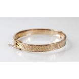 An early 20th century 9ct gold hinged bangle, with engraved scrolling decoration to front, 8mm wide,