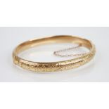 An early 20th century 9ct gold hinged bangle, of oval form with engraved floral decoration, dated