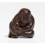 NETSUKE: SITTING DARUMA SITTING IN TATEHIZA WITH ONE KEE UP. Japan. 19. Jh. Dark wood, probably