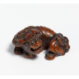 NETSUKE: RECUMBENT SHISHI WITH MOVEABLE BALL IN THE MOUTH. Japan. 18th c. Reddish brown wood, carved