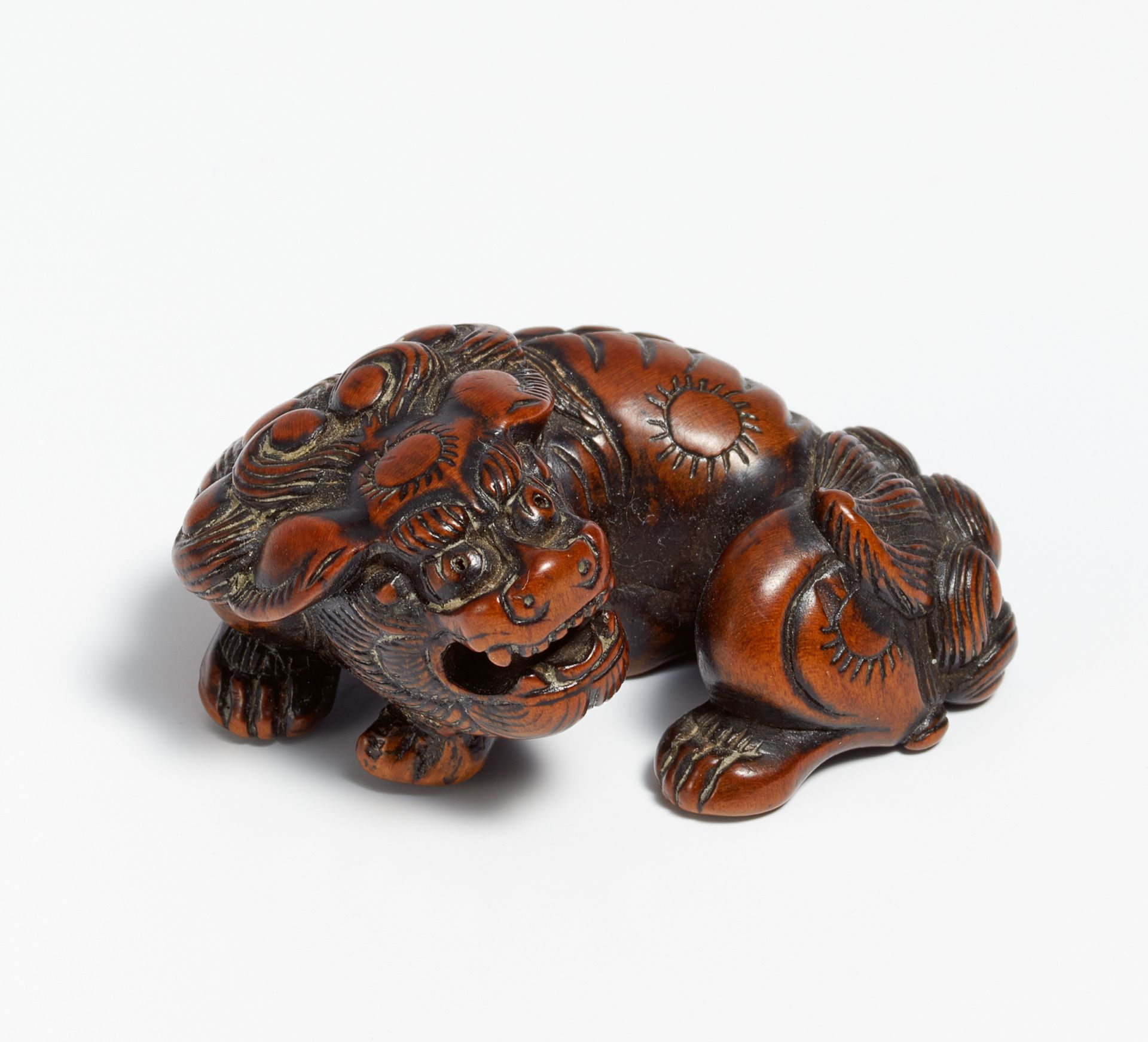 NETSUKE: RECUMBENT SHISHI WITH MOVEABLE BALL IN THE MOUTH. Japan. 18th c. Reddish brown wood, carved