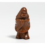 NETSUKE: STANDING DARUMA IN ROBE WITH FLY WHISK. Japan. 19th c. Wood, carved. H.5.2cm. Condition A/