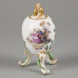 A porcelain egg on legs and a leaf-shaped knob, decorated with classical scenes on both sides, marke