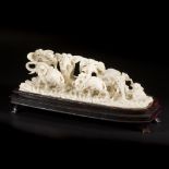 An ivory group depicting a herd of elephants, on a wooden base. China, circa 1920.