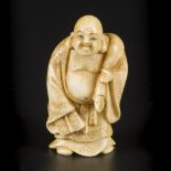 An ivory okimono of a laughing/ happy Buddha as traveller, Japan, Meiji period, ca. 1910.