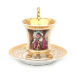 A gilded porcelain cup on claw-feet with saucer and a polychrome decoration of a lady in medieval co