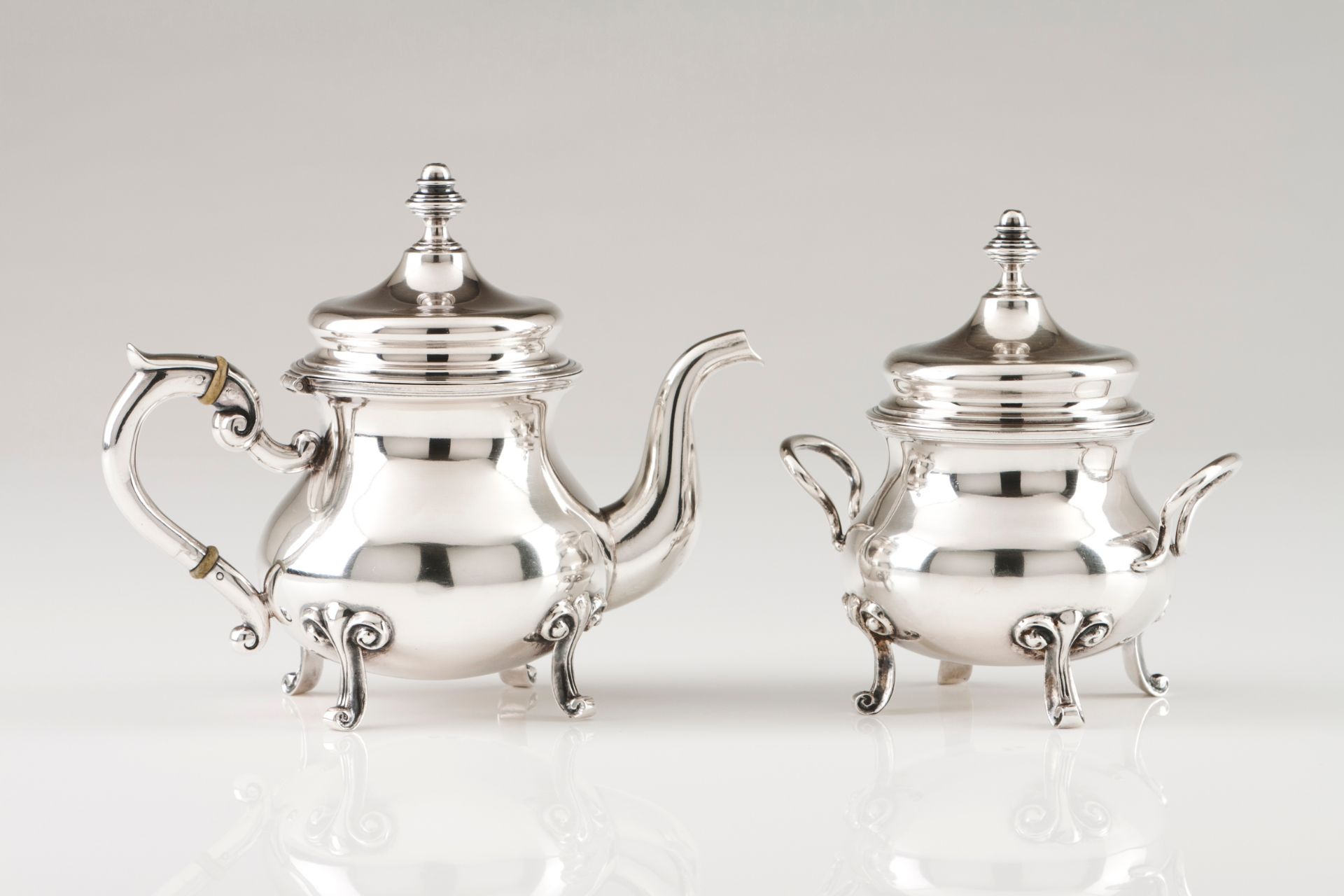 A small teapot and sugar bowlPortuguese silver Plain body on four scroll feet and volute handles
