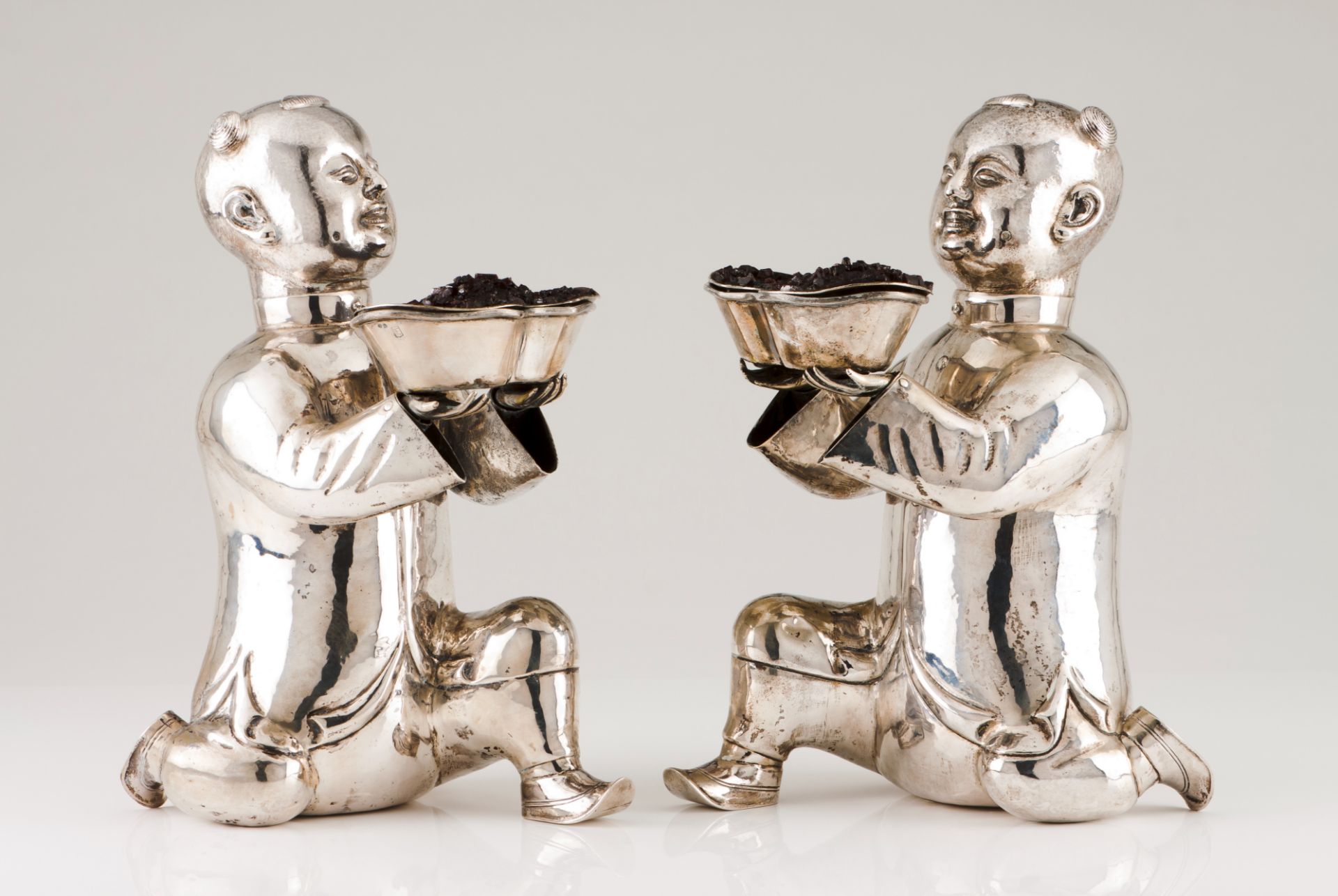 A pair of Luiz Ferreira laughing boysSilver Moulded sculptures holding votive offering bowls