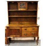 An Arts and Crafts oak dresser, the sideboard base asymmetric with drawers and cupboard, plate