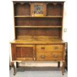 An Arts and Crafts oak dresser, the sideboard base asymmetric with drawers and cupboard, plate