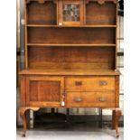 An Arts and Crafts oak dresser, the sideboard base asymmetric with drawers and cupboard, plate