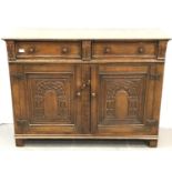 An early 20th Century oak sideboard in the Priory style with carved cupboard doors and two short