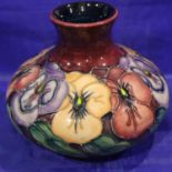 Moorcroft red ground bulbous vase in the Pansy pattern. H: 10 cm. No cracks, chips or visible