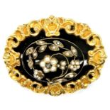 An oval memorial brooch with raised central plaque of black enamel overset with arching stems and