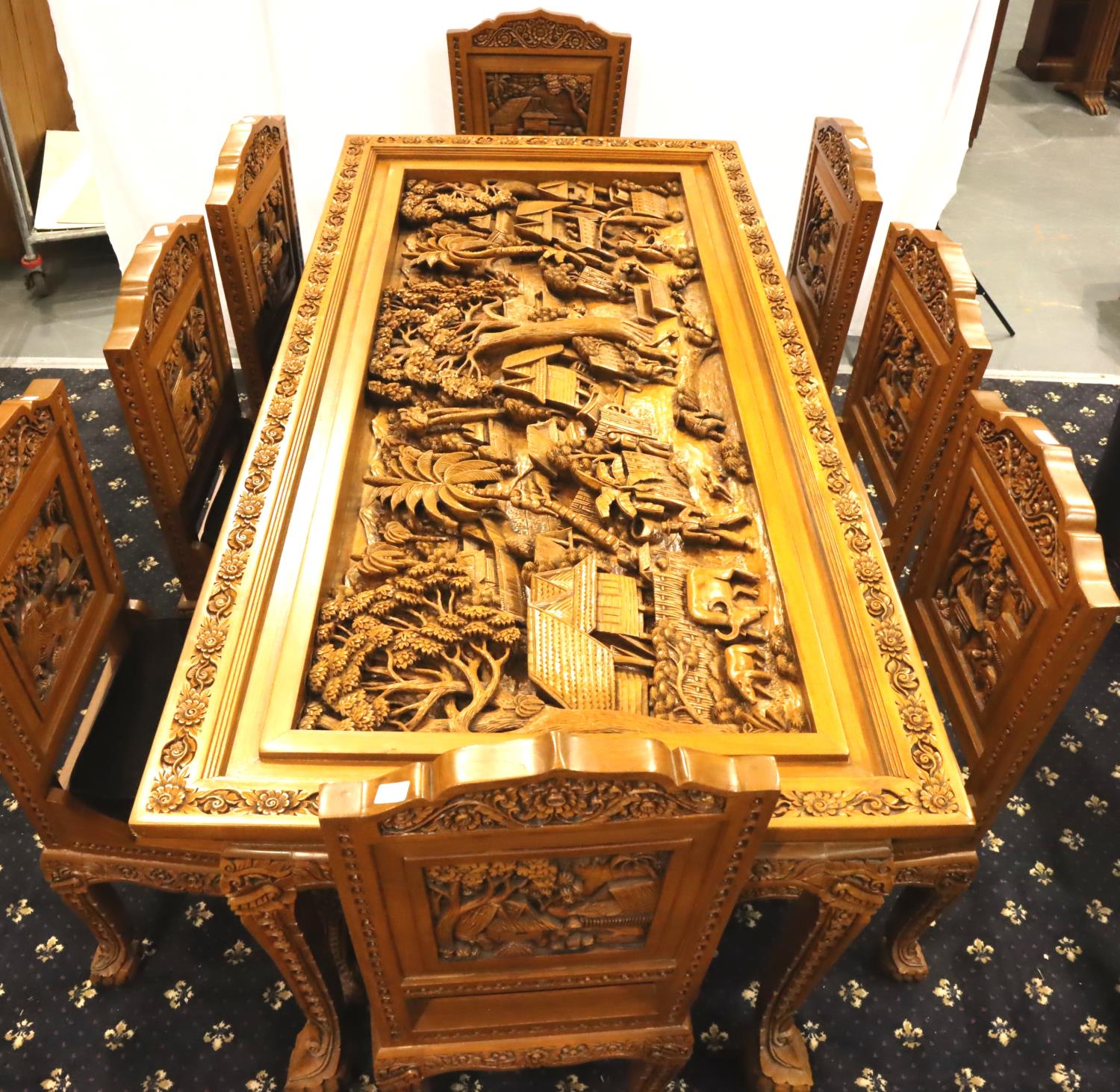 A deeply carved substantial Oriental hardwood dining table with plate glass top displaying figures