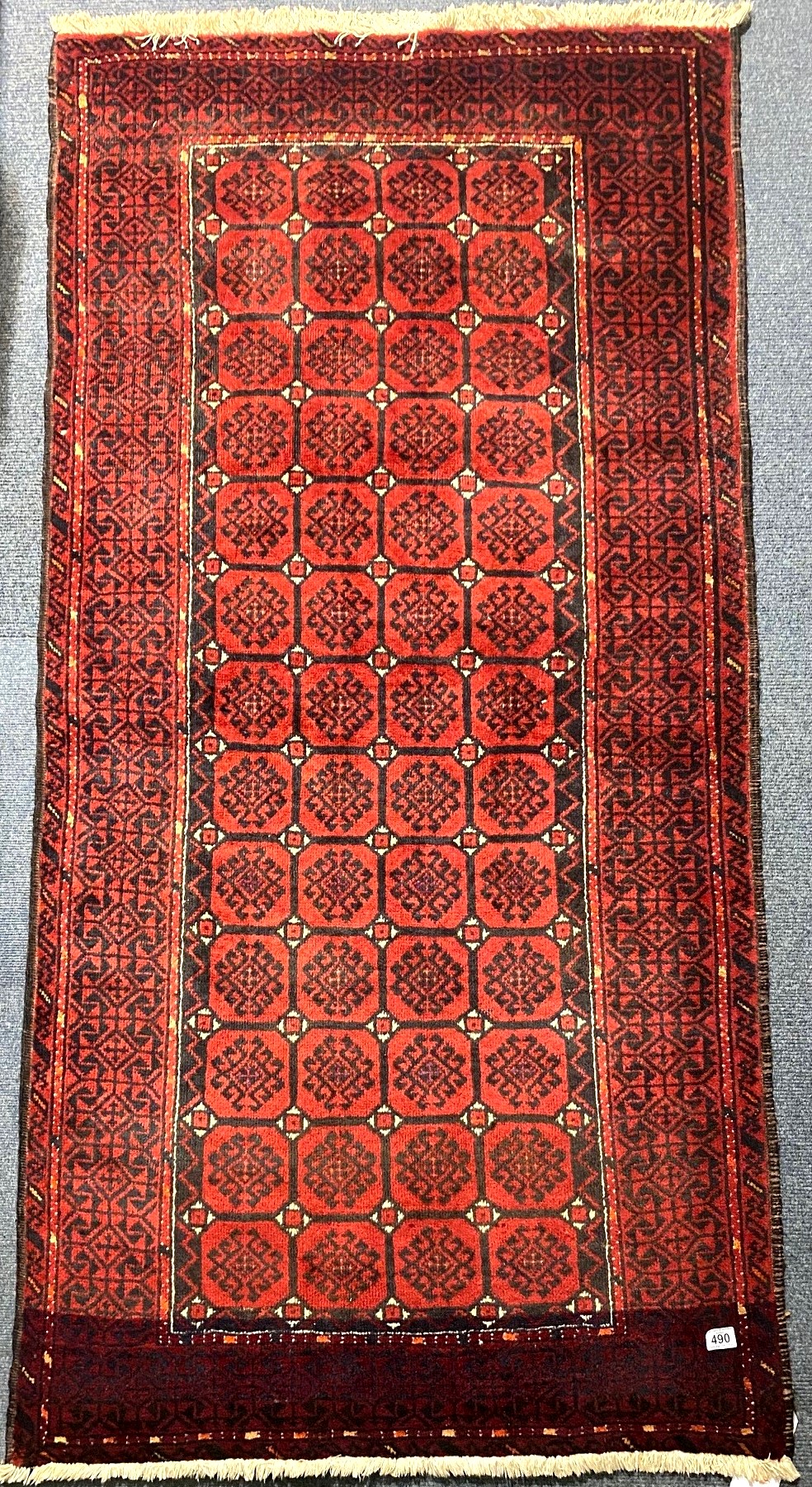 Red ground woollen fringed rug with 52 panels and geometric design border, 200 x 100 cm. Not