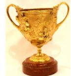 A 19th century gilt bronze cup decorated in relief with mythical creatures on a rough marble base,