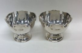 A pair of circular silver bowls with shaped rims.