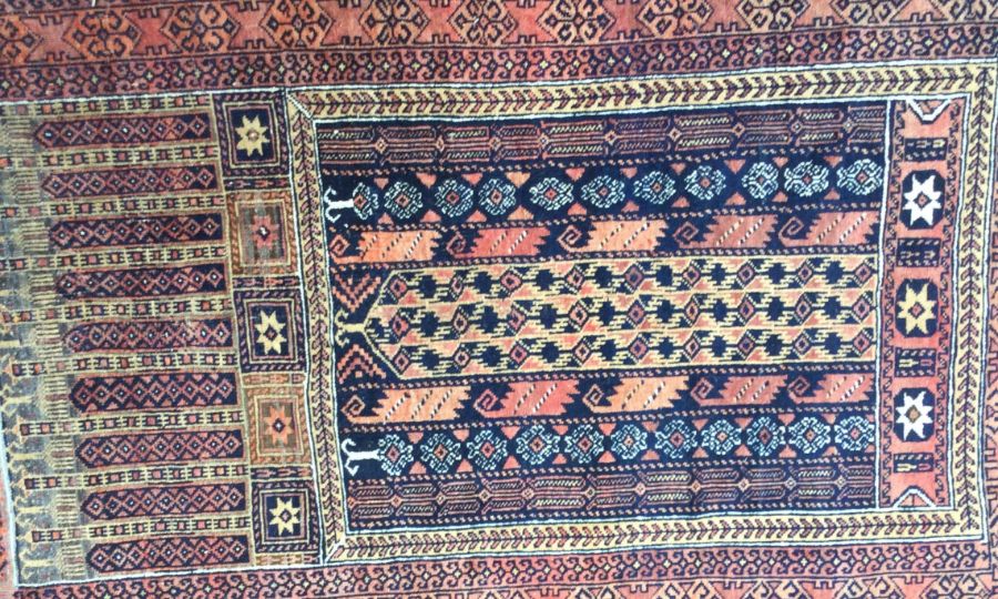 An old red ground rug. Est. £20 - £30.