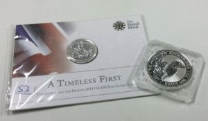 A silver 1 oz coin together with a 'Timeless First