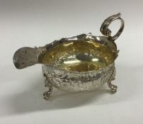 A chased silver sauce boat decorated with flowers.