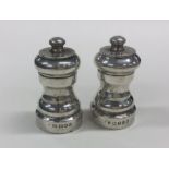 A pair of circular silver pepper grinders of shape
