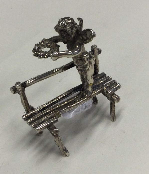 A silver figure of a cherub on a bench with outstr