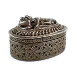 An Anglo Indian metalware box and cover of oval form decorated with a lion at rest,