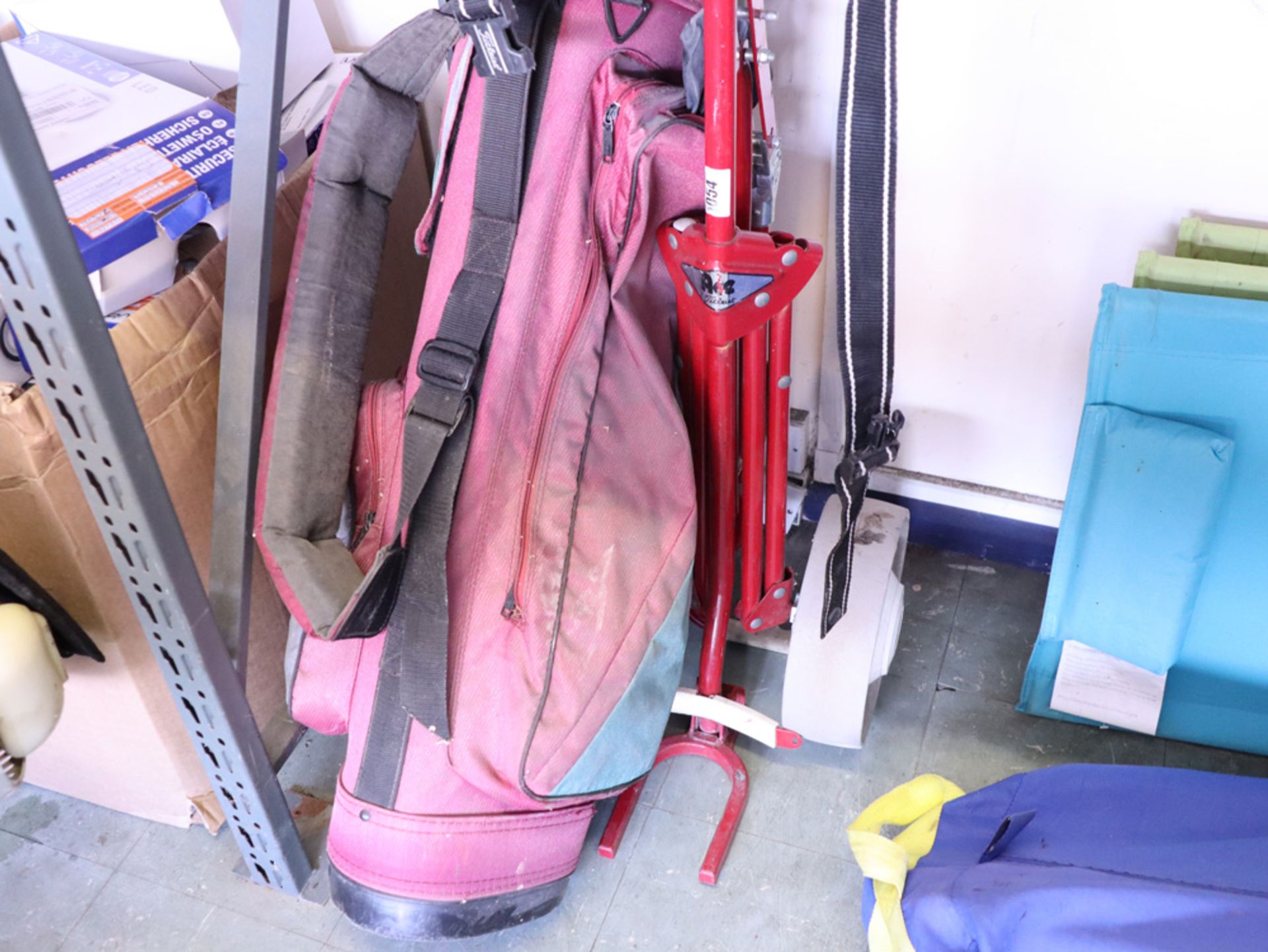 Red Titleist golf bag with small quantity of various clubs and manual trolley