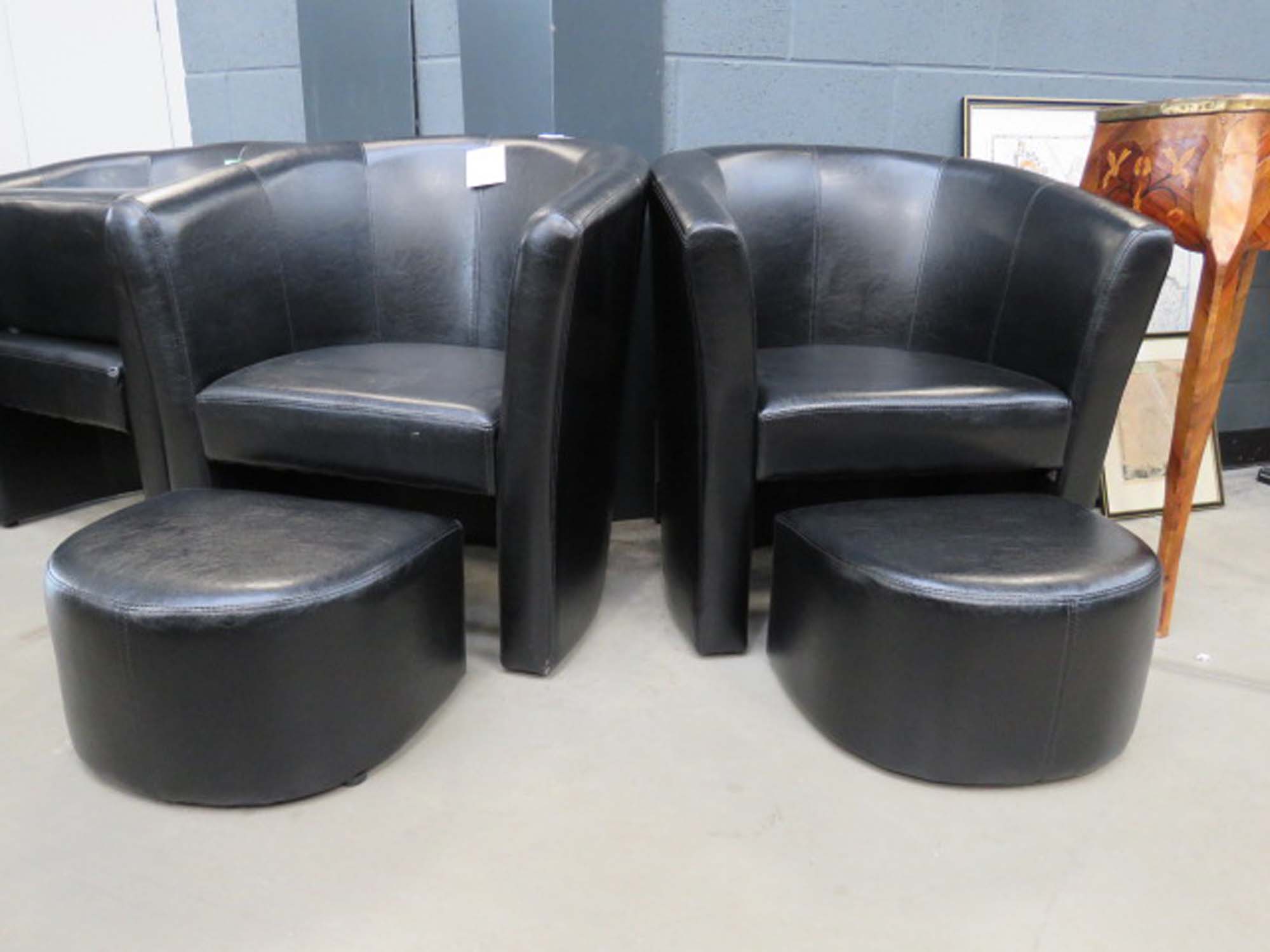 Pair of black leather effect tub chairs with footstools