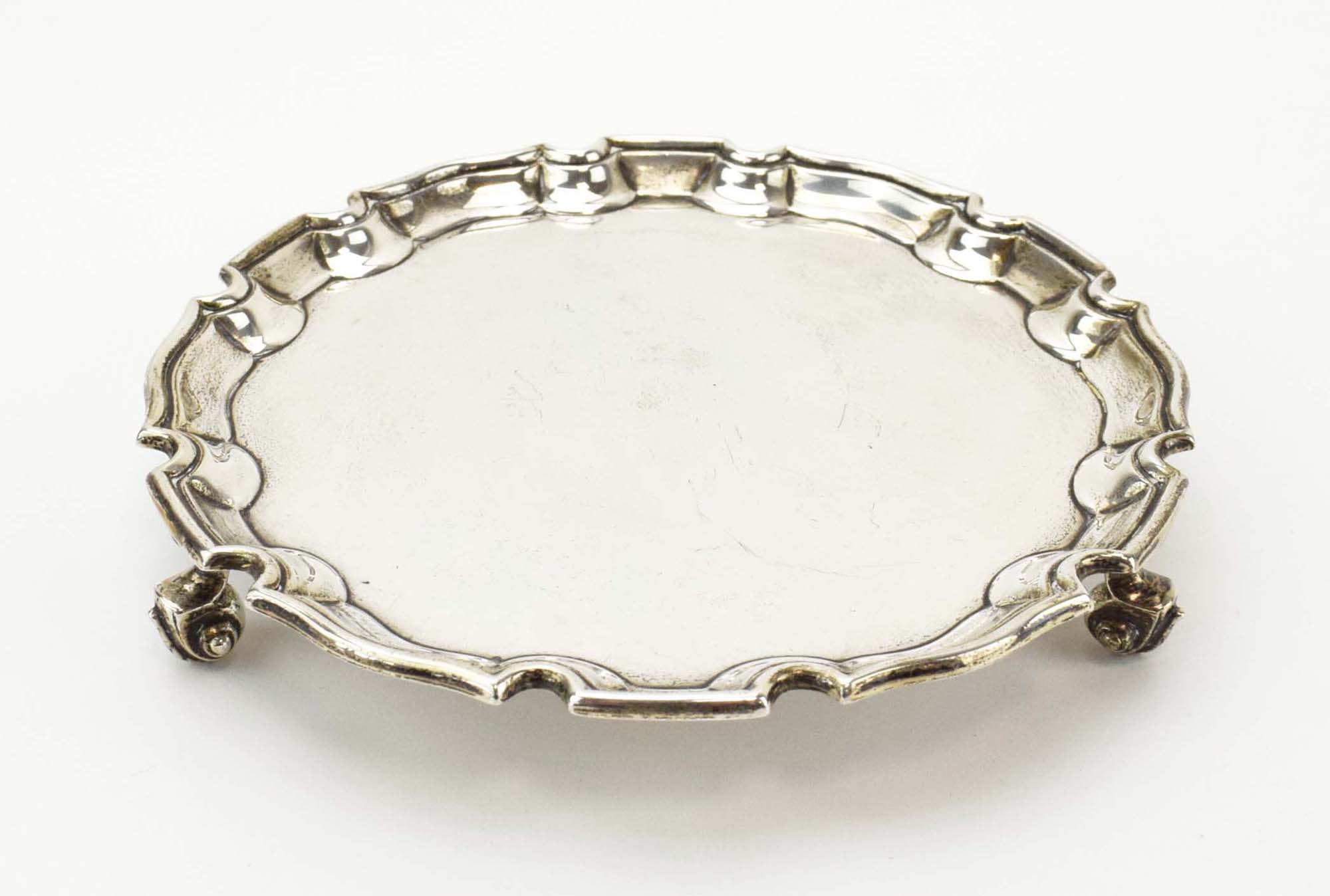 An early 20th century silver card tray of circular form with piecrust border on three scrolled feet,