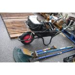 Black metal wheelbarrow containing tools incl. hammers, brush head, spade, rake, etc.