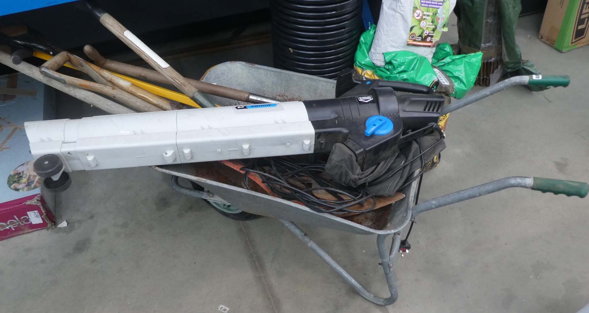 Wheelbarrow containing MacAllister leaf blower, forks, bulb planter, and weeder