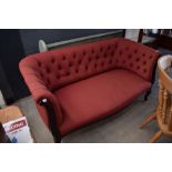 Red button backed 2 seater armchair on darkwood supports