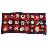 A tartan scarf holding twenty-five Scottish metalwares cap badges including The Cameronians,