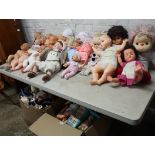 Table top of various toy dolls with 2 boxes of dolls and cuddly animals