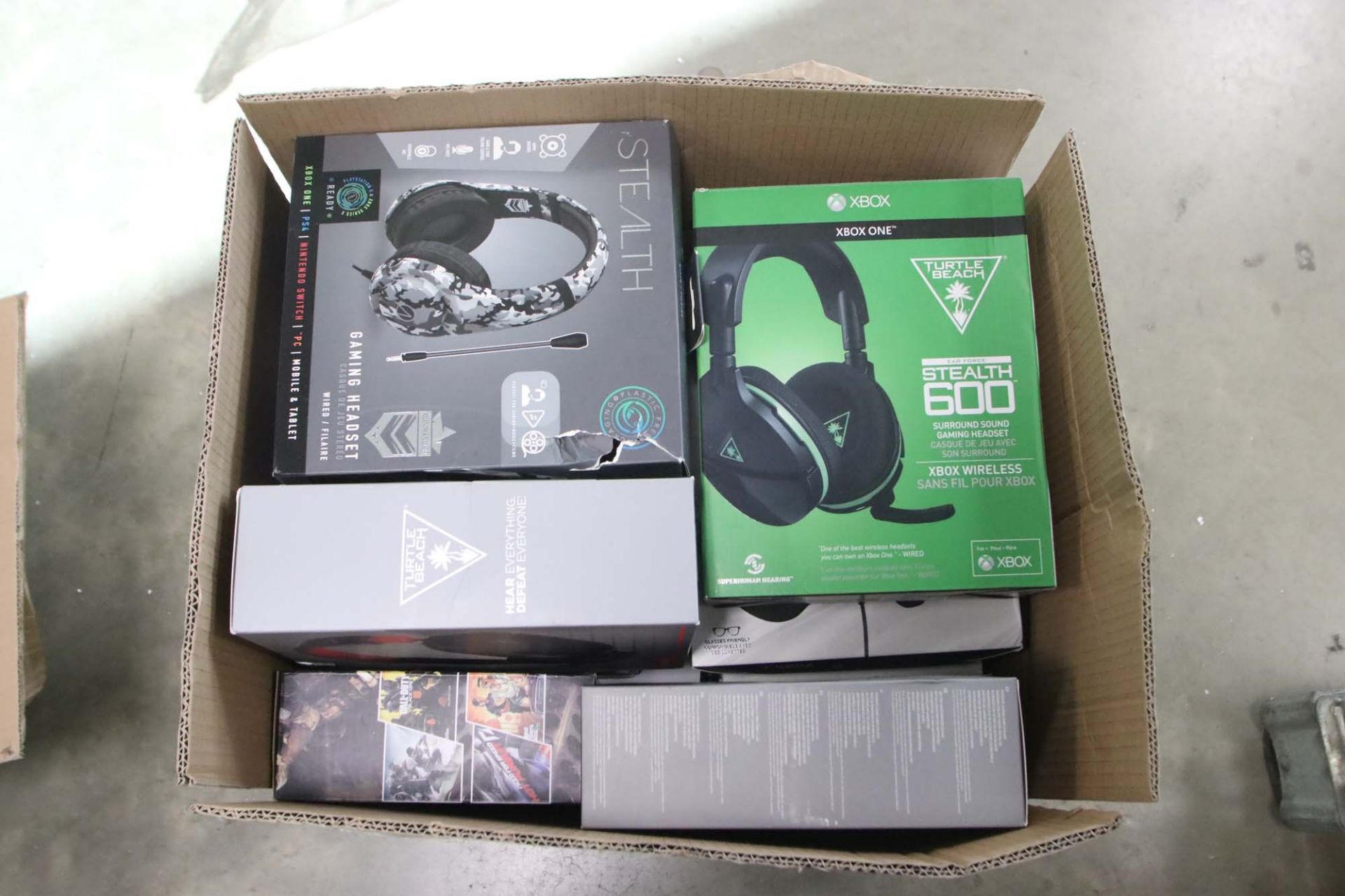 Box containing a variety of headsets, gaming controllers and other electrical sundries