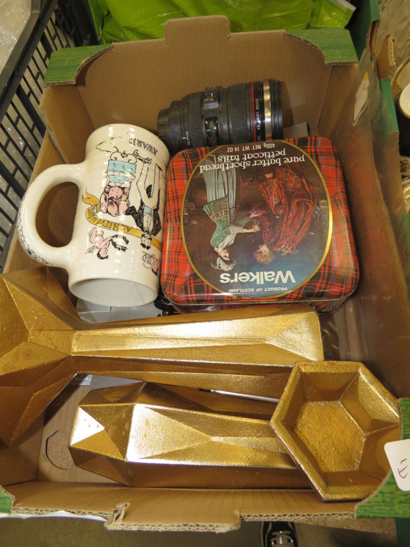 Box containing a camera lens, shortbread tin, 2 candlesticks and an ale mug