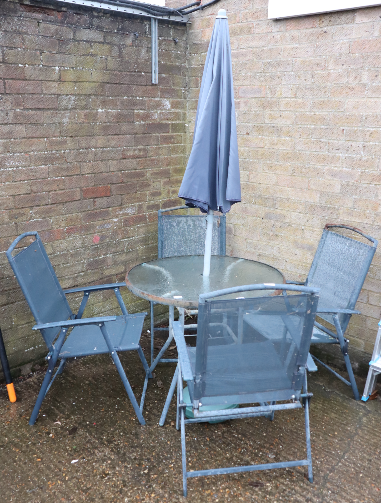 Circular glass top garden table with 4 blue metal mesh garden chairs and parasol