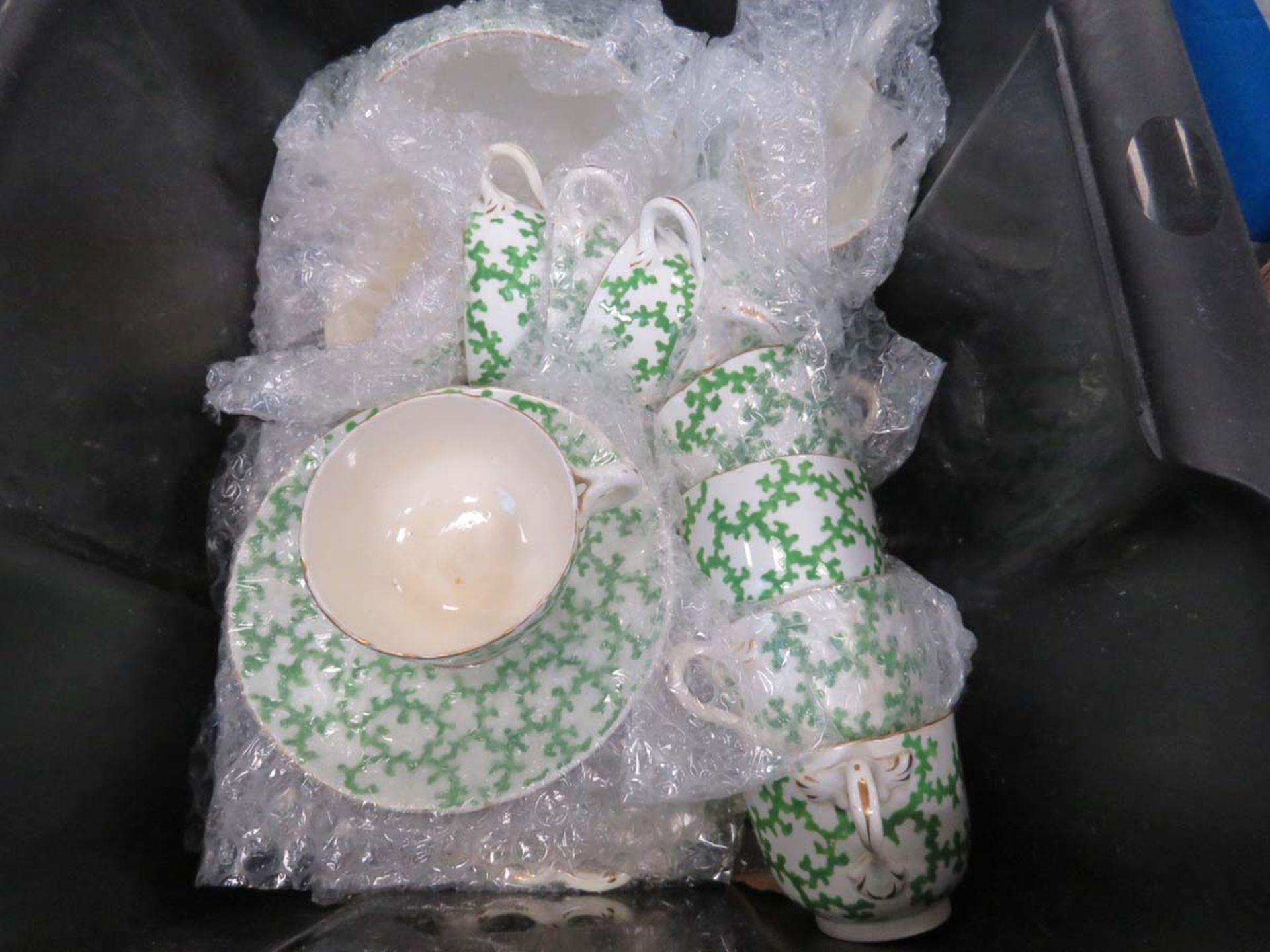 Box containing green glazed cups and saucers with green hand decorated pattern