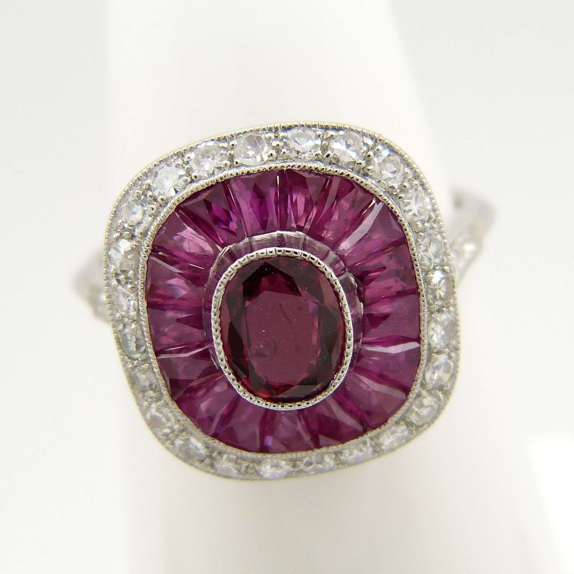 A platinum ring set with central oval-cut and surrounding calibre-cut rubies and round brilliant-cut - Image 3 of 6